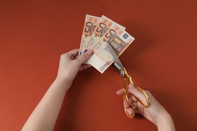 Photo of Woman cutting euro banknotes on brown background, top view