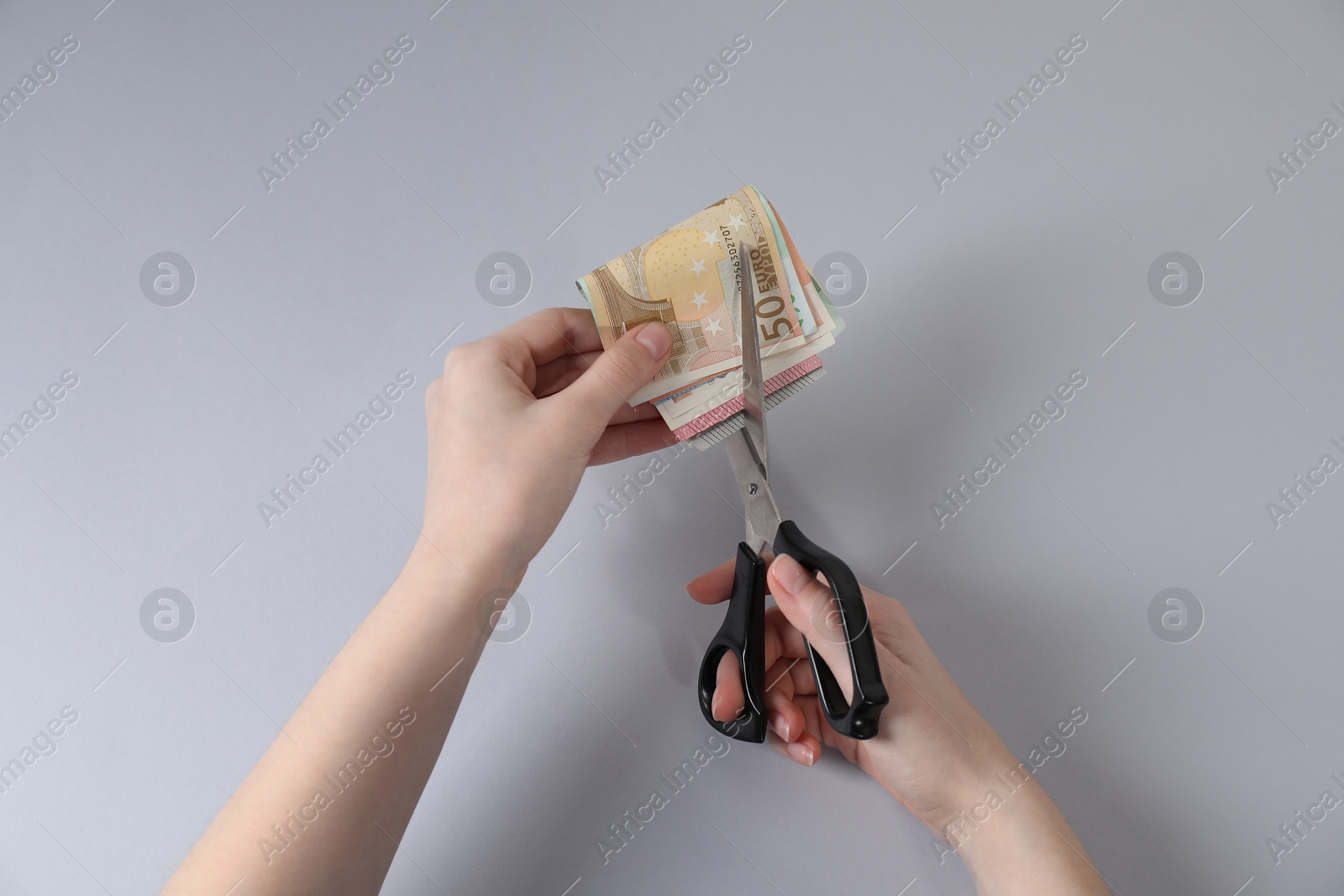 Woman cutting euro banknotes on gray background, top view Photo of Woman cutting euro banknotes on gray background, top view