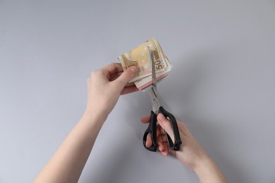 Photo of Woman cutting euro banknotes on gray background, top view