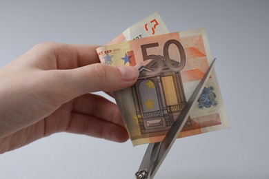 Photo of Woman cutting euro banknote on gray background, closeup