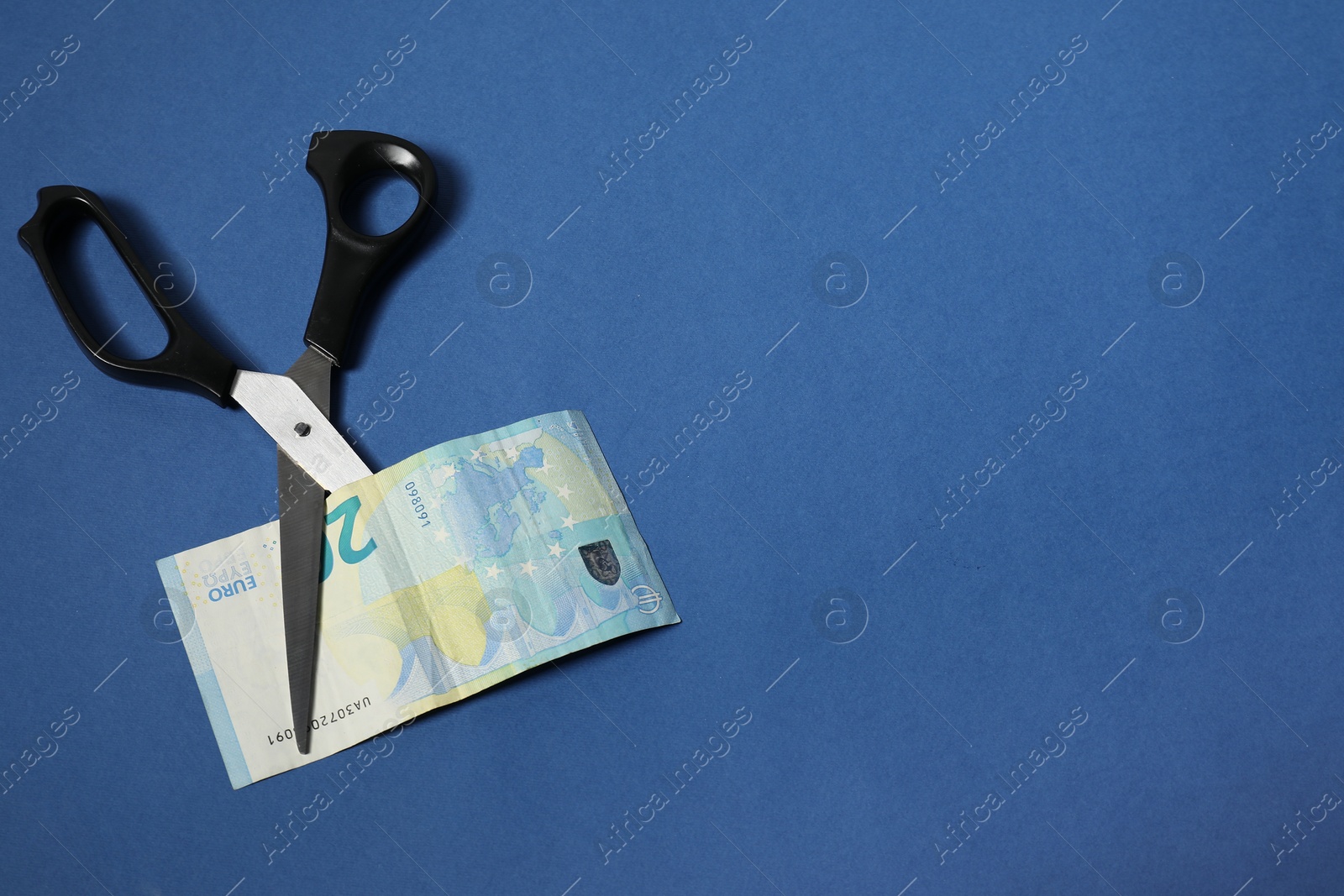 Photo of Scissors with euro banknote on blue background, top view. Space for text