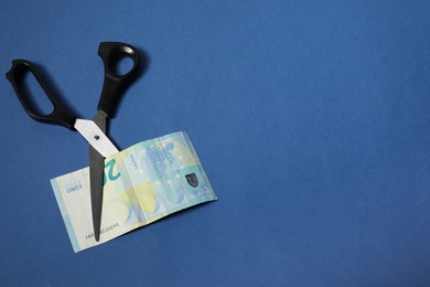 Photo of Scissors with euro banknote on blue background, top view. Space for text