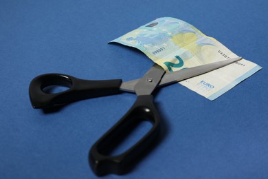 Photo of Scissors with euro banknote on blue background, closeup