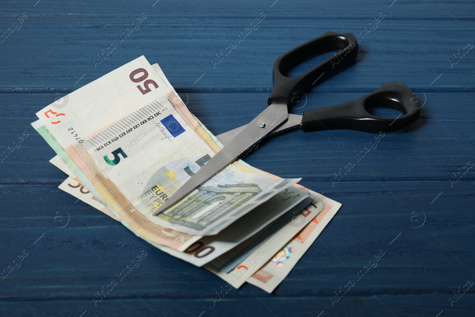 Photo of Euro banknotes and scissors on blue wooden table