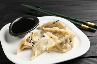 Photo of Delicious gyoza dumplings with sesame seeds served on black wooden table, closeup