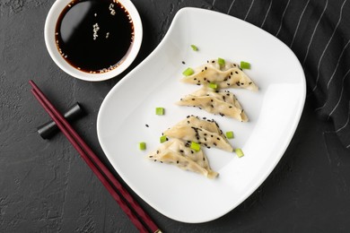 Photo of Delicious gyoza dumplings with chives and sesame seeds served on black table, top view