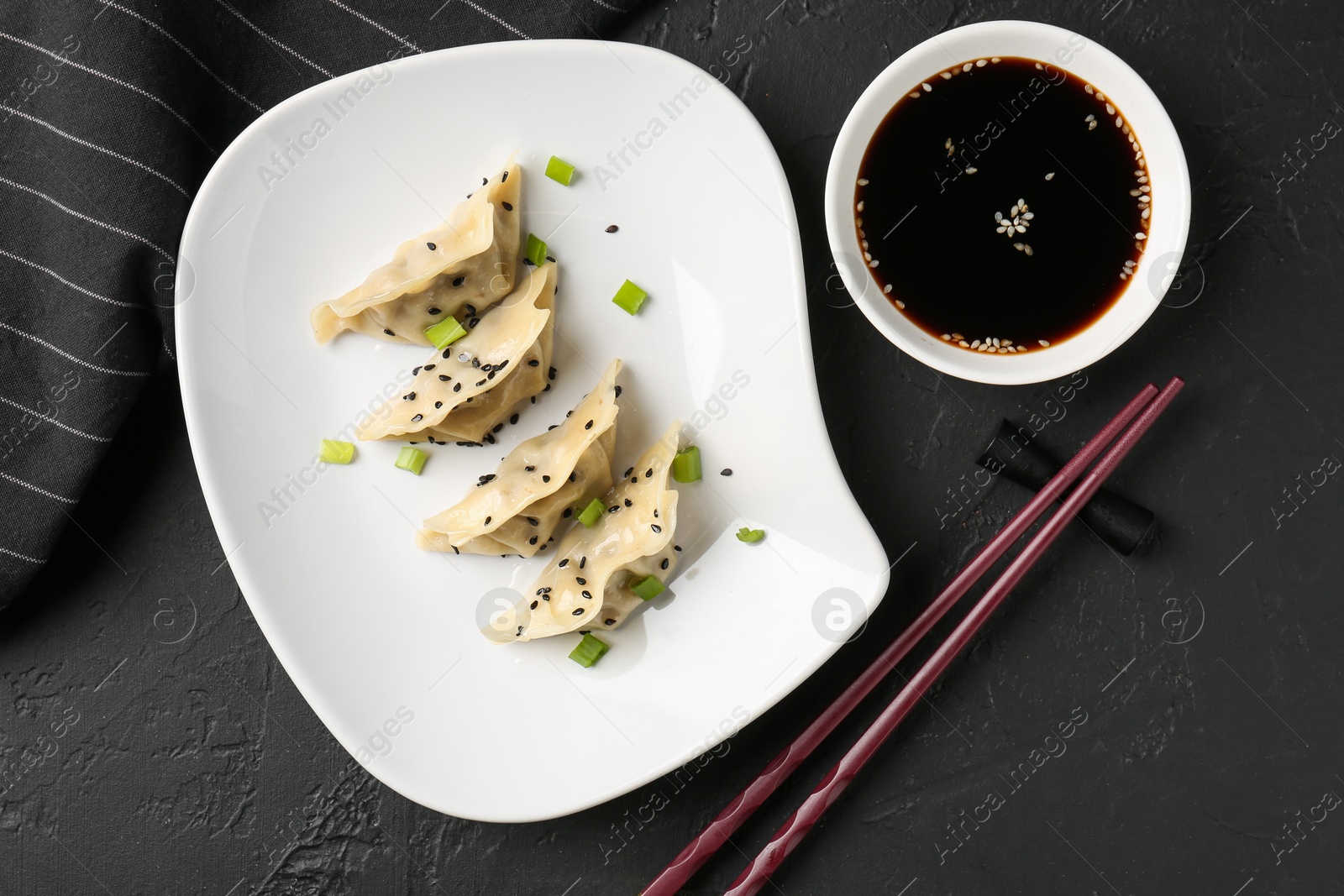 Photo of Delicious gyoza dumplings with chives and sesame seeds served on black table, top view