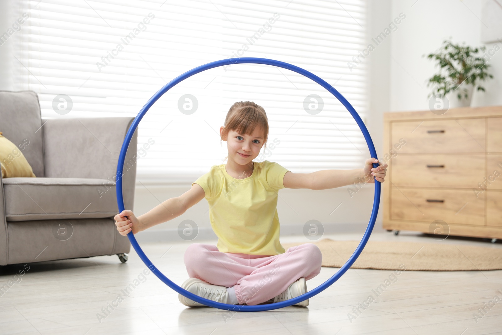 Photo of Cute little girl with hula hoop on floor at home