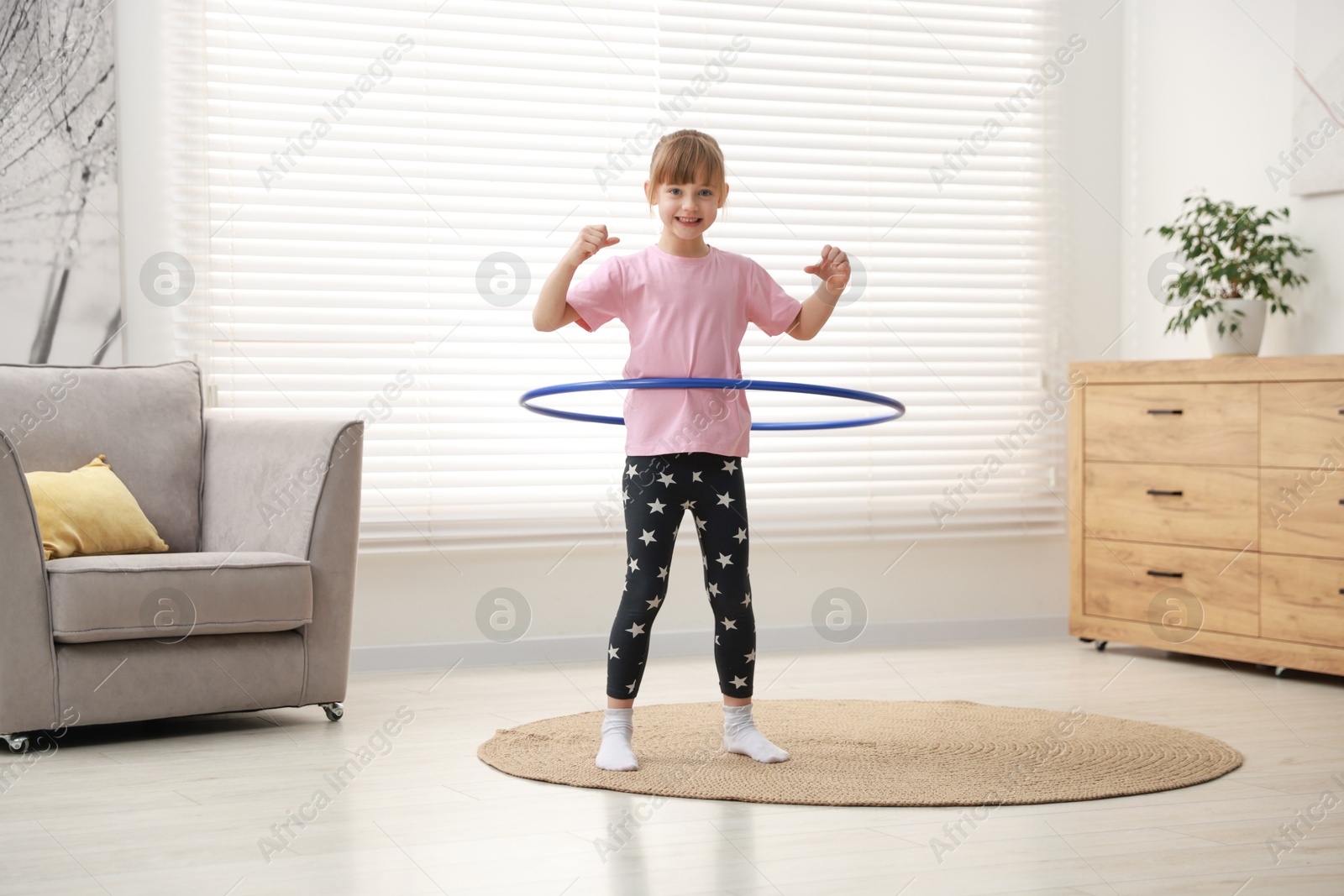 Photo of Cute little girl exercising with hula hoop at home