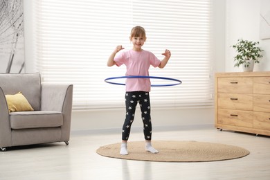 Photo of Cute little girl exercising with hula hoop at home