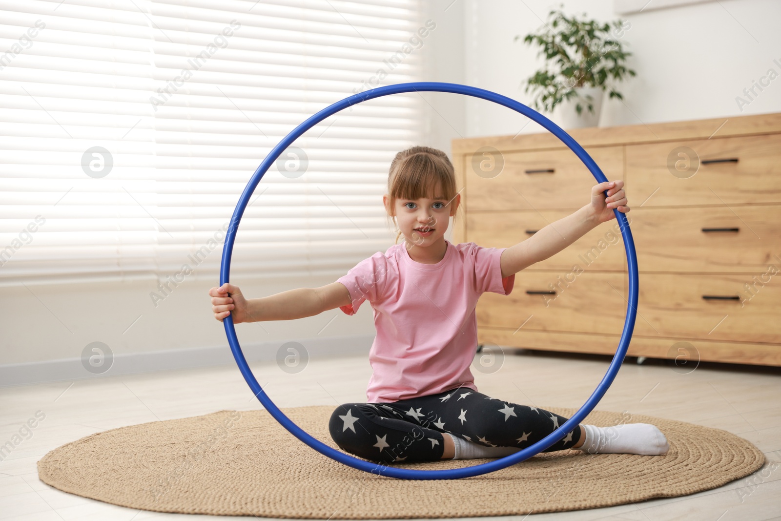 Photo of Cute little girl with hula hoop on floor at home