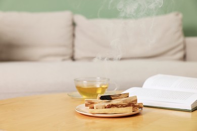 Photo of Palo santo sticks, book and tea on wooden table indoors, space for text