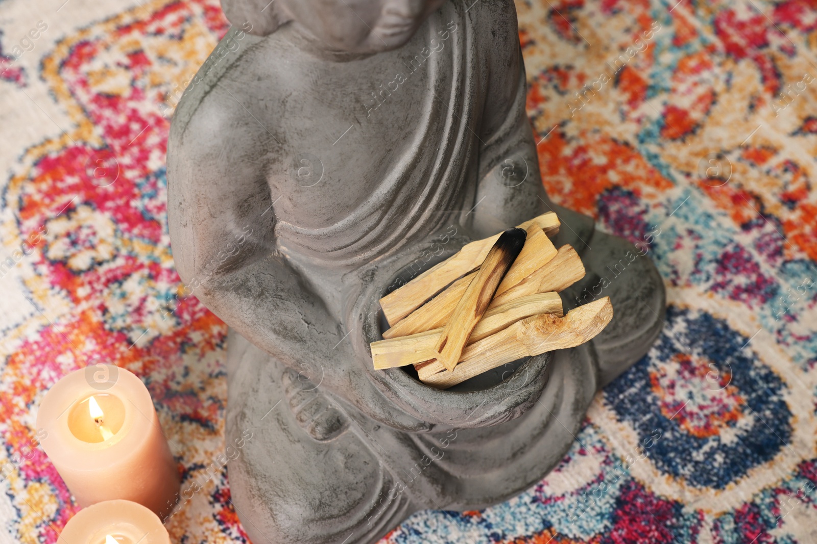 Photo of Buddha statue with palo santo sticks and burning candles on rug indoors, above view