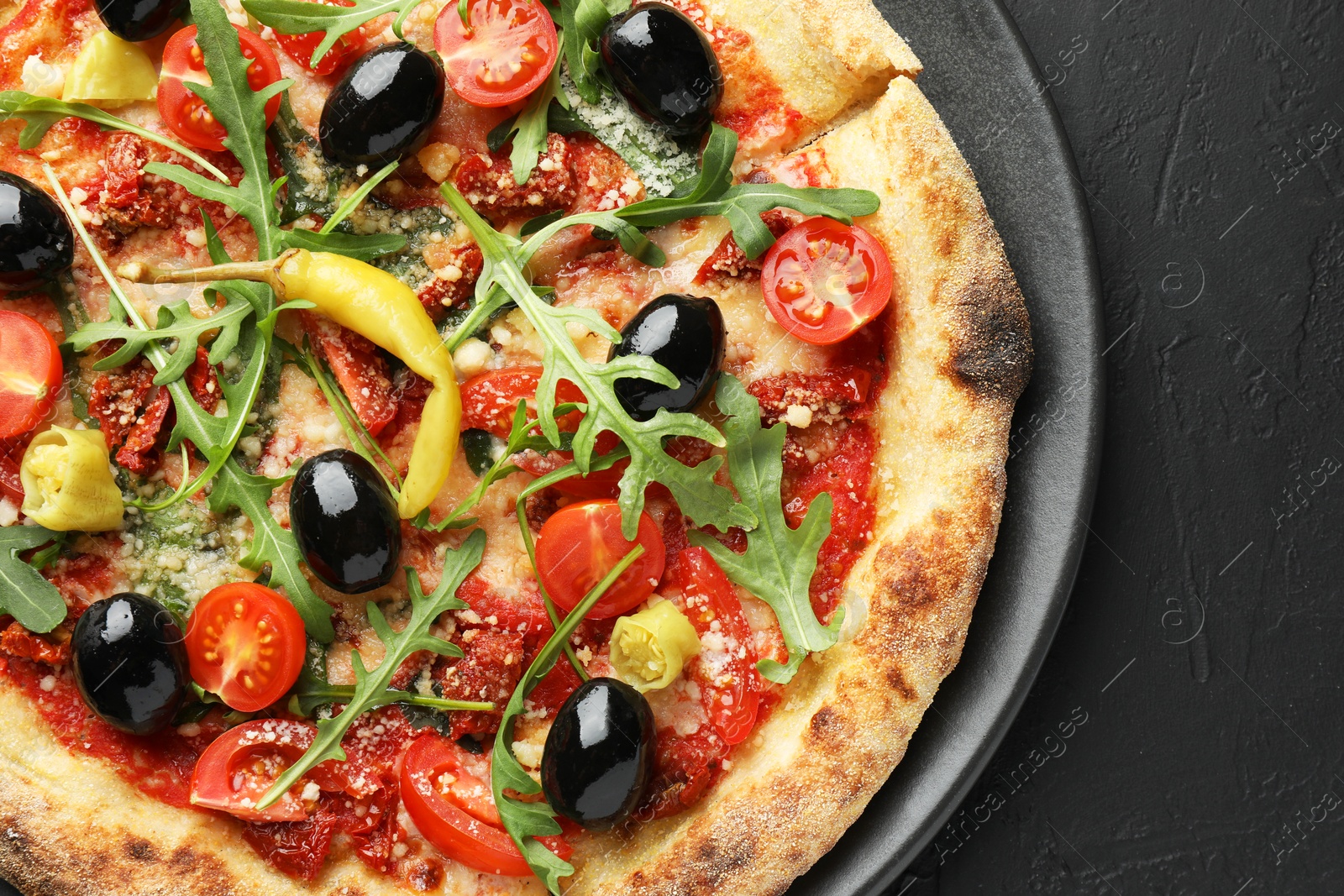 Photo of Tasty pizza with tomatoes, olives, chili and arugula on black table, top view