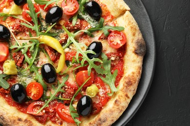 Tasty pizza with tomatoes, olives, chili and arugula on black table, top view