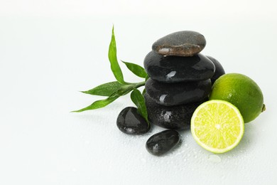 Photo of Spa composition with limes, massage stones and green leaves on wet surface, space for text