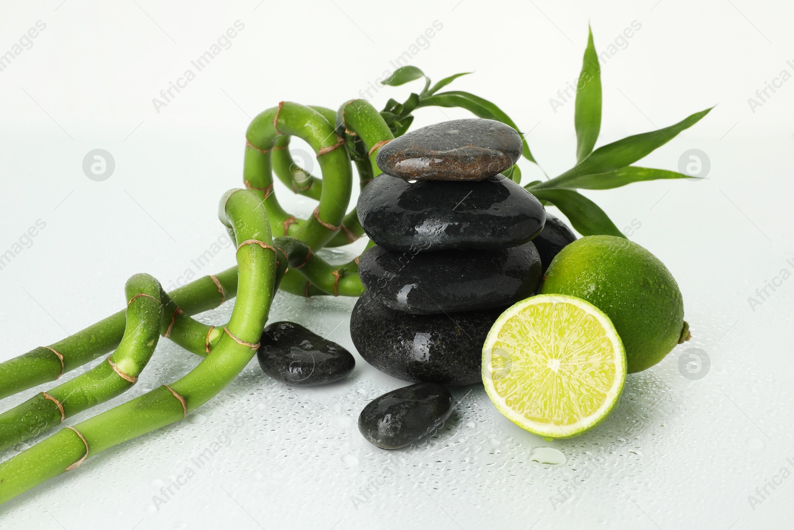 Spa composition with limes, massage stones and bamboo stems on wet surface Photo of Spa composition with limes, massage stones and bamboo stems on wet surface