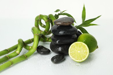 Photo of Spa composition with limes, massage stones and bamboo stems on wet surface