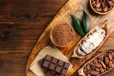 Photo of Cocoa pods with beans and chocolate on wooden table, flat lay. Space for text