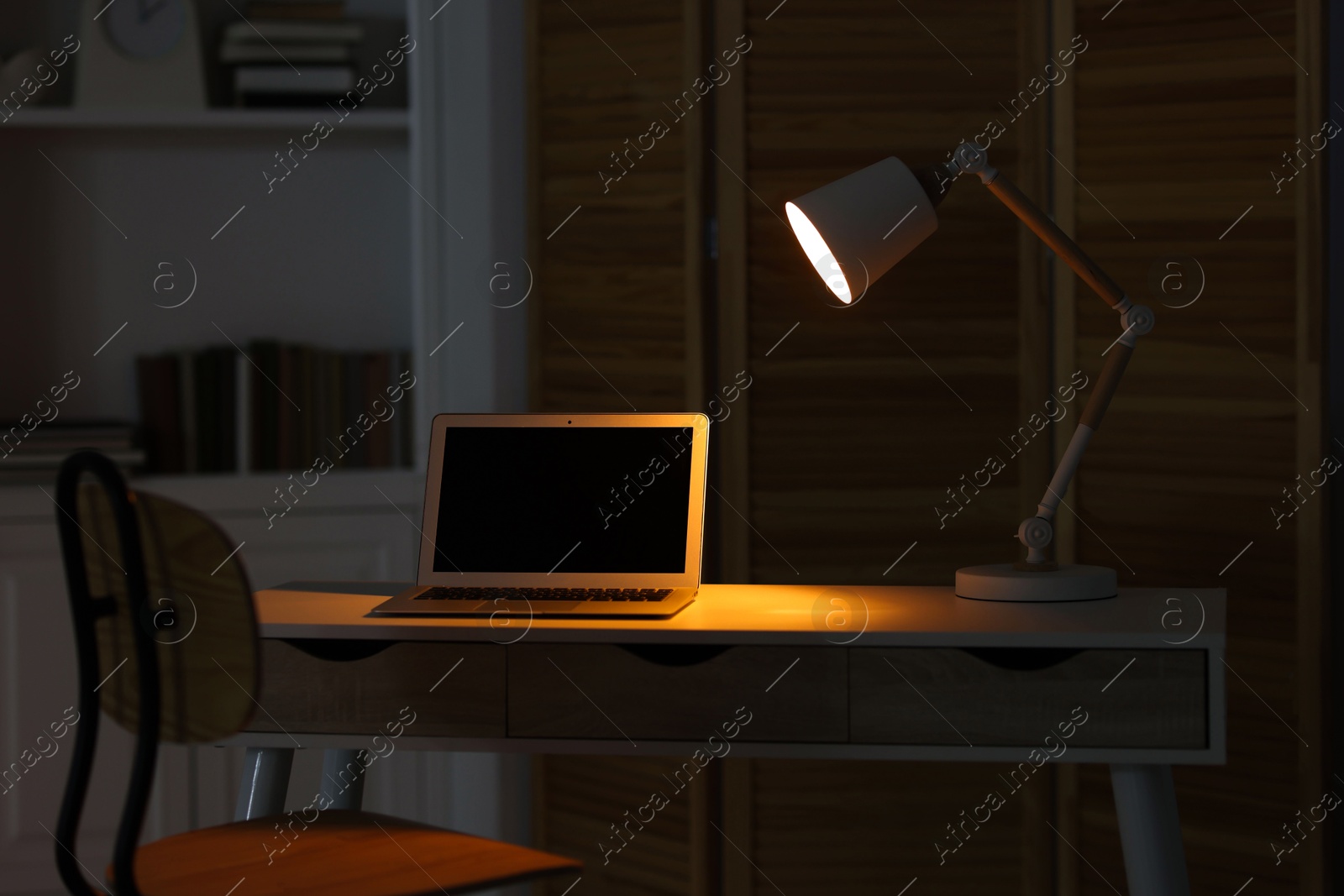 Comfortable workplace with laptop and lamp on table indoors Photo of Comfortable workplace with laptop and lamp on table indoors