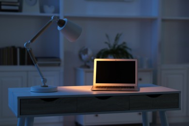 Photo of Comfortable workplace with laptop and lamp on table indoors