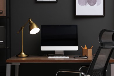 Photo of Comfortable workplace with computer and lamp on wooden desk in home office