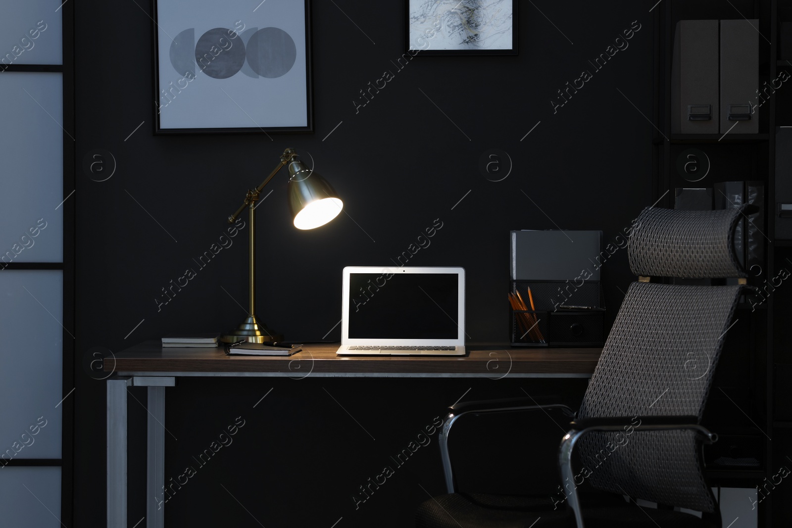 Comfortable workplace with laptop and lamp on wooden desk at home office in evening Photo of Comfortable workplace with laptop and lamp on wooden desk at home office in evening