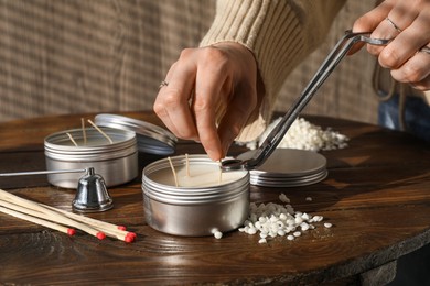 Photo of Woman cutting soy candle wick with trimmer at wooden table, closeup