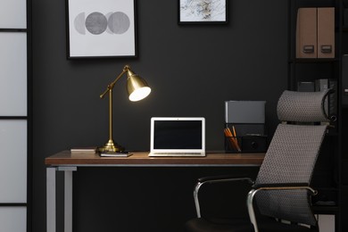 Photo of Home office. Comfortable workplace with laptop and lamp on wooden desk in room