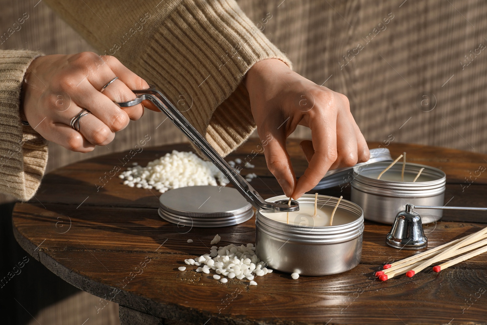 Photo of Woman cutting soy candle wick with trimmer at wooden table, closeup