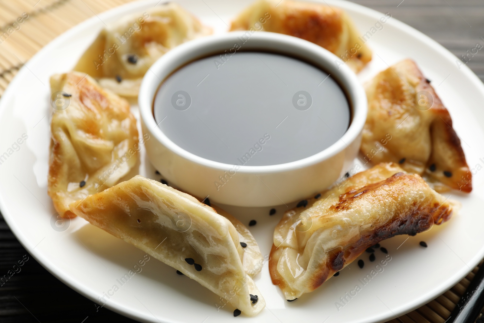 Photo of Delicious fried gyoza dumplings with sesame seeds and soy sauce on table, closeup