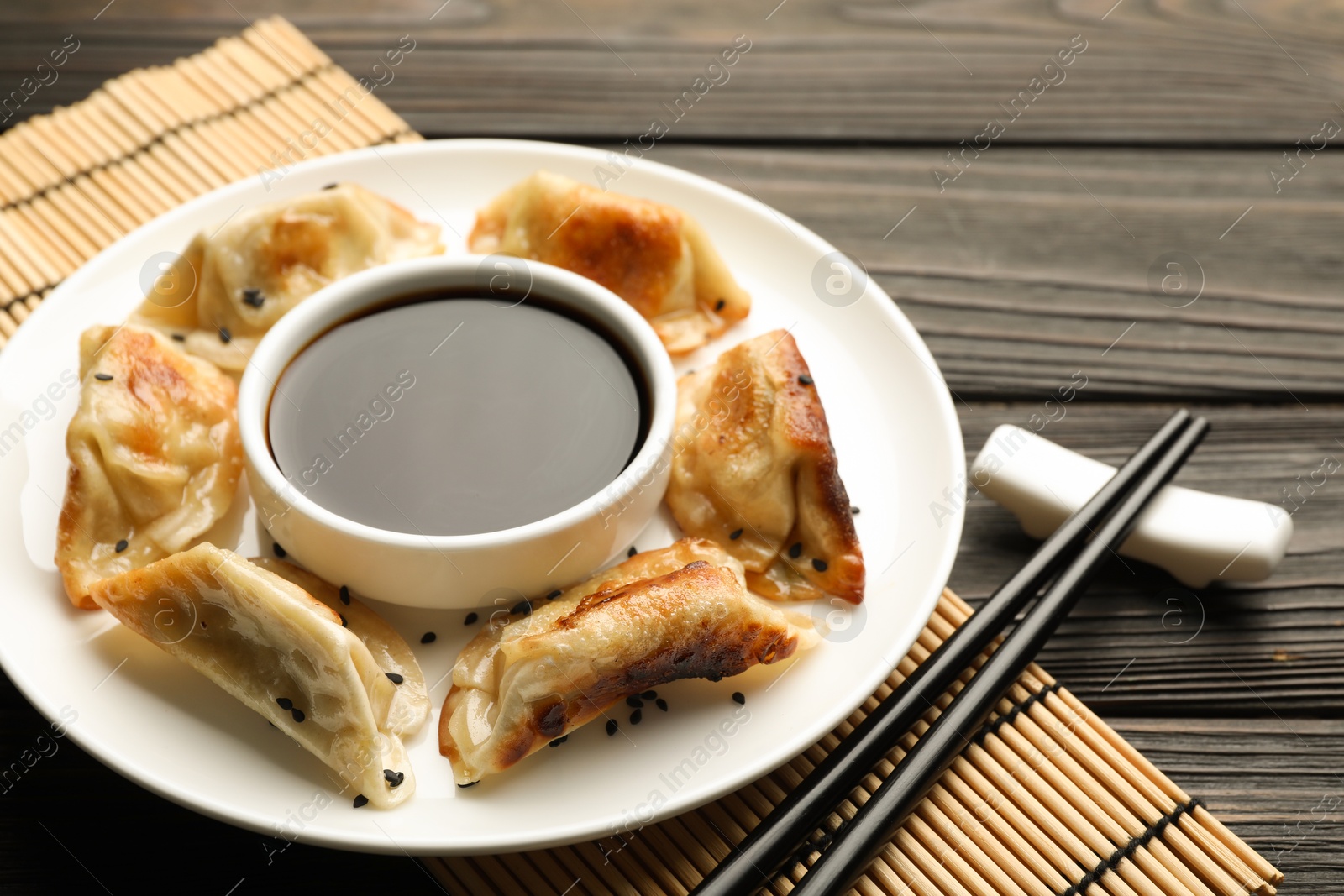 Photo of Delicious fried gyoza dumplings with sesame seeds served on wooden table, closeup