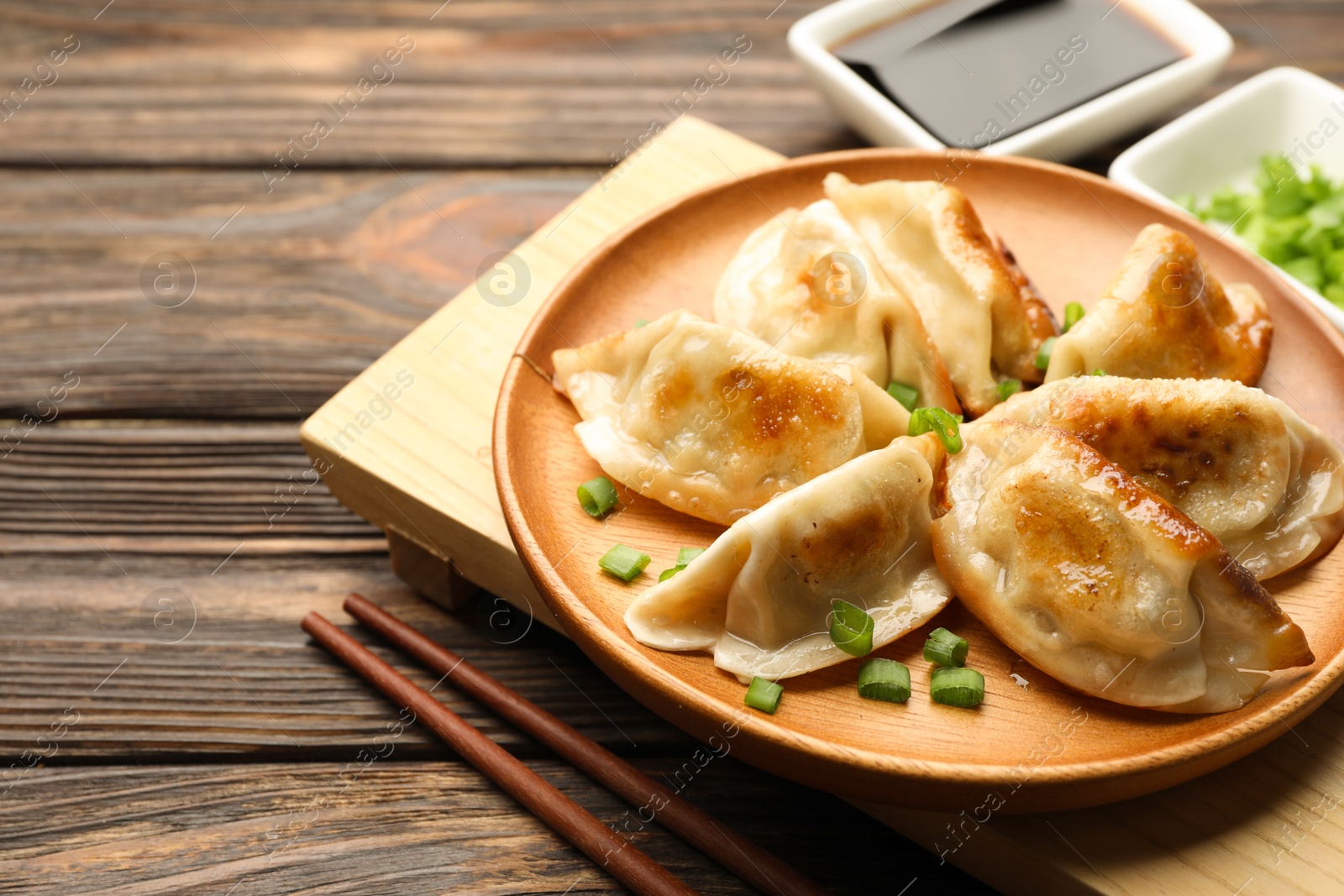 Photo of Delicious fried gyoza dumplings with green onions served on wooden table, closeup