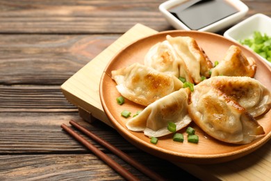 Delicious fried gyoza dumplings with green onions served on wooden table, closeup