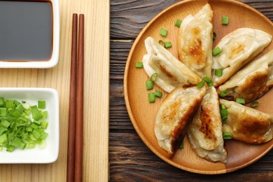 Delicious fried gyoza dumplings with green onions served on wooden table, flat lay