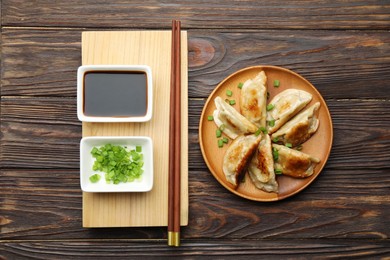 Photo of Delicious fried gyoza dumplings with green onions served on wooden table, flat lay