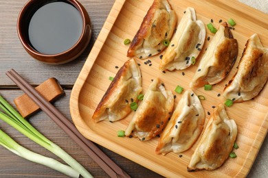 Delicious fried gyoza dumplings with sesame seeds served on wooden table, flat lay