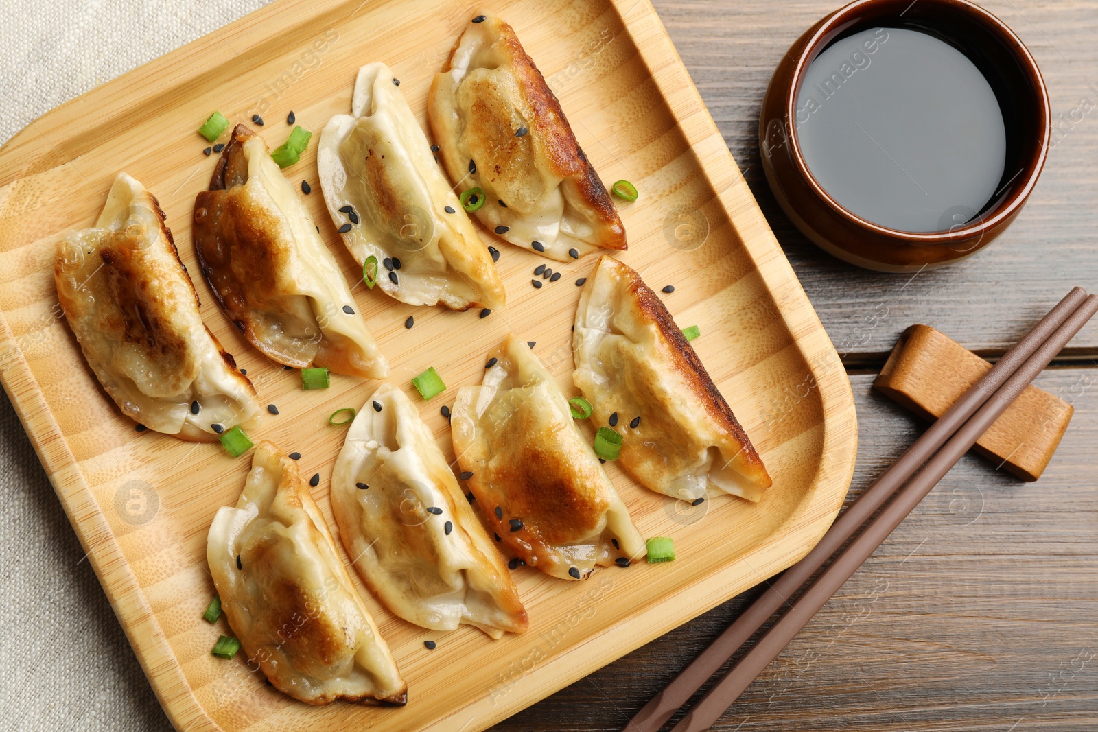 Photo of Delicious fried gyoza dumplings with sesame seeds served on wooden table, flat lay