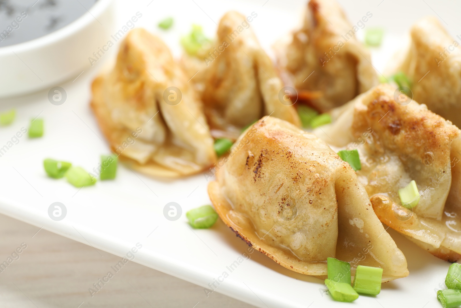 Photo of Fried gyoza dumplings with green onions and soy on white table, closeup