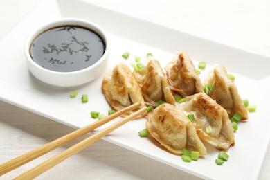 Photo of Delicious fried gyoza dumplings with green onions served on white wooden table, closeup