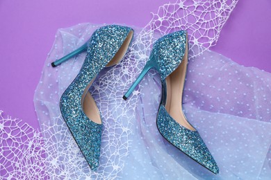 Photo of Beautiful high heeled shoes, lace ribbon and tulle cloth on violet background, flat lay