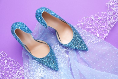 Photo of Beautiful high heeled shoes, lace ribbon and tulle cloth on violet background, flat lay