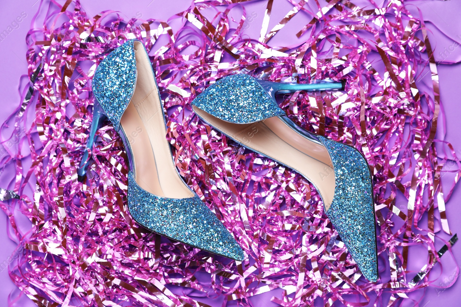 Photo of Beautiful high heeled shoes and bright tinsel on violet background, flat lay