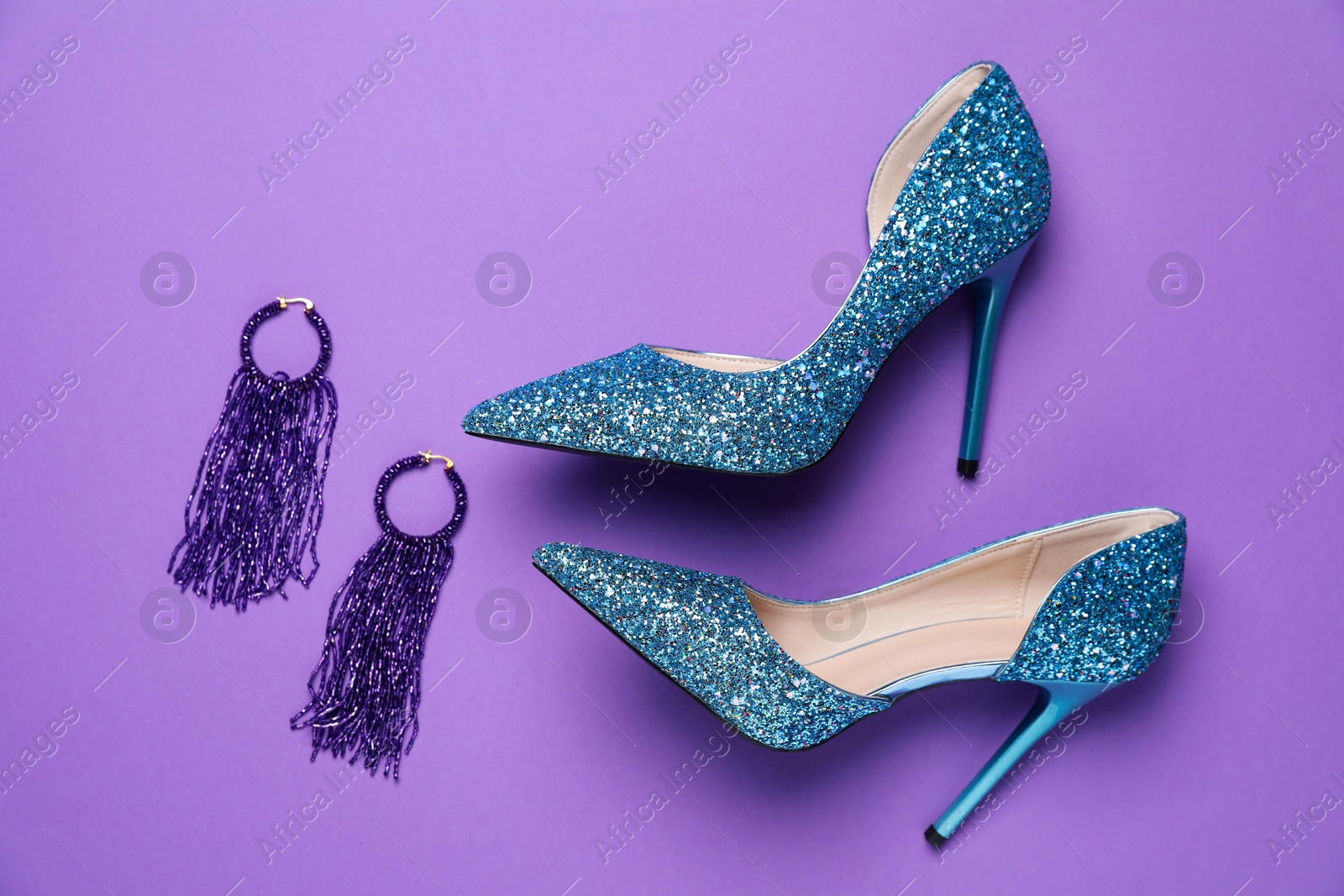 Photo of Beautiful high heeled shoes and earrings on violet background, flat lay