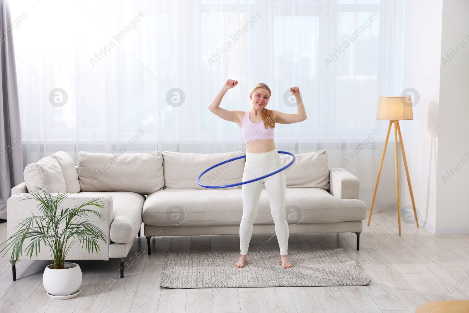 Photo of Beautiful young woman exercising with hula hoop at home