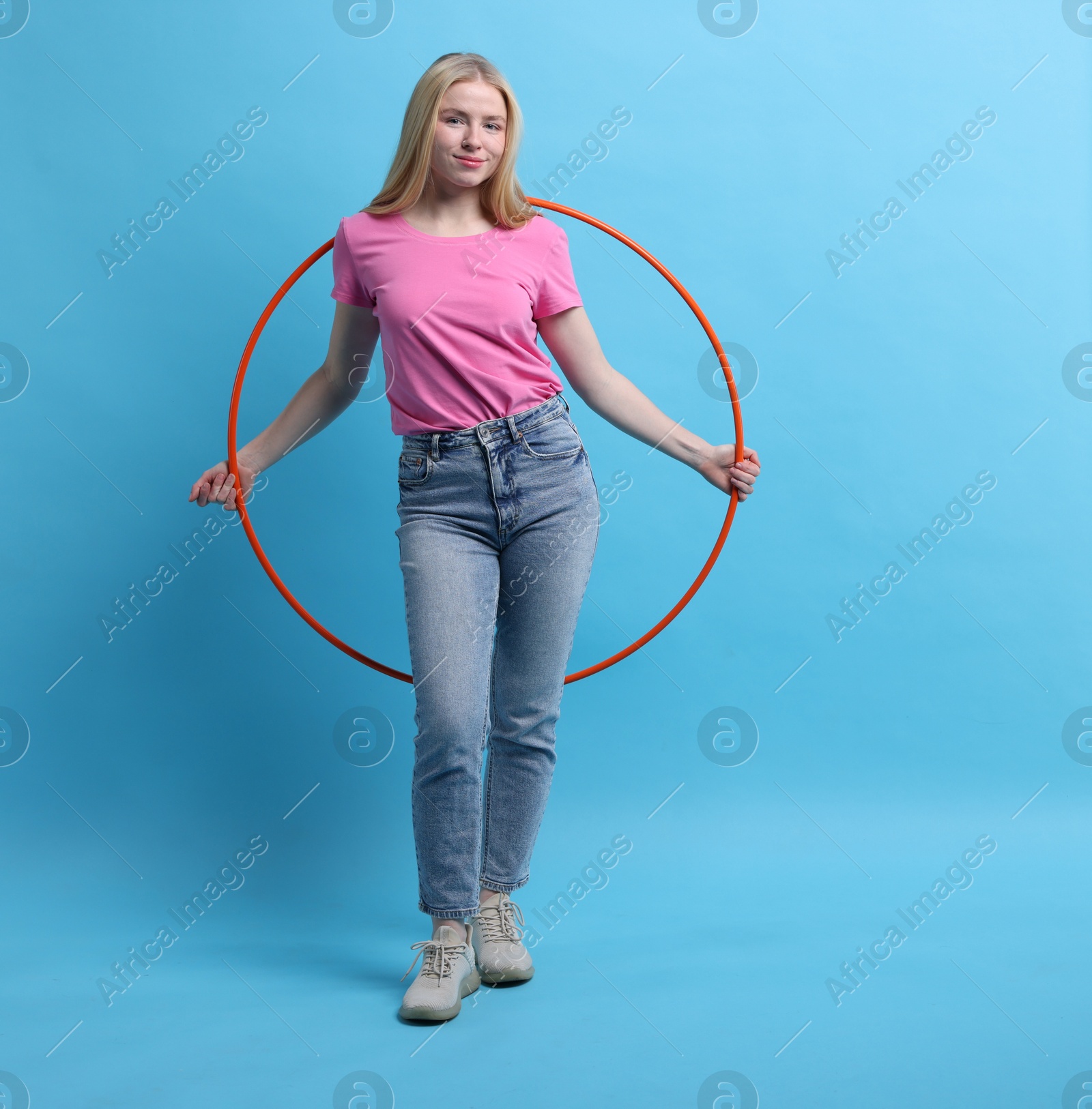 Photo of Beautiful young woman with hula hoop on light blue background, space for text