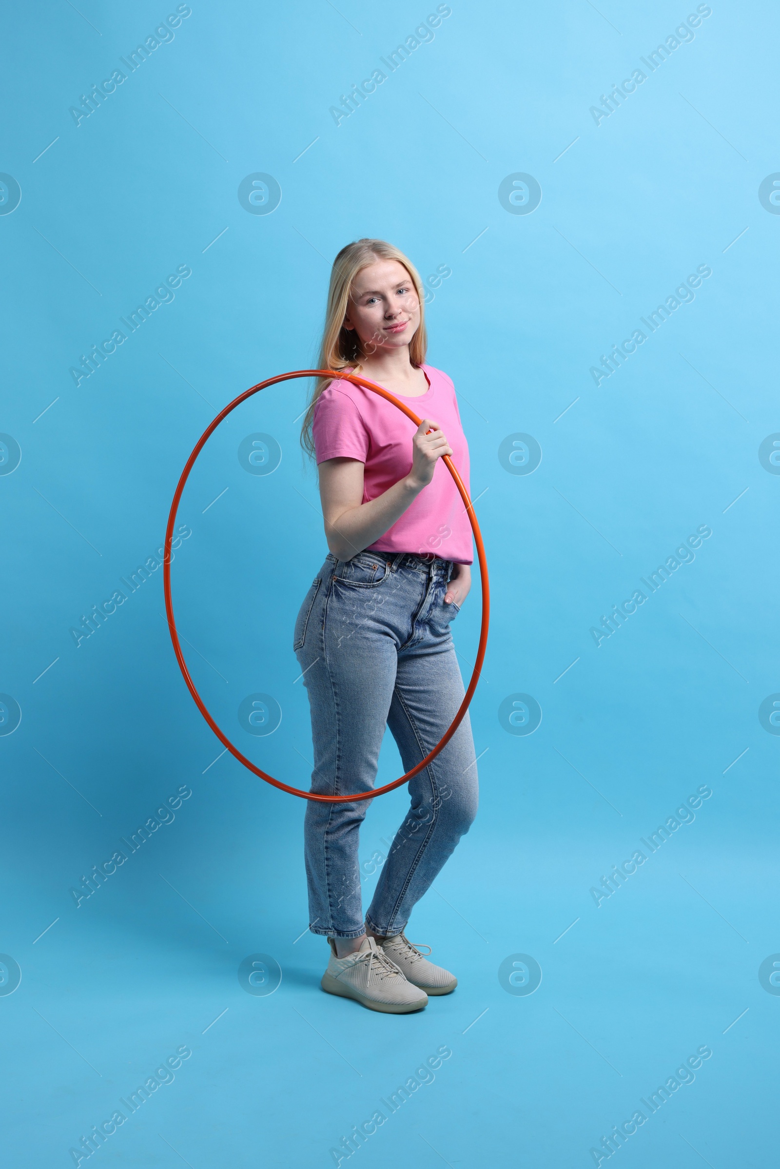 Photo of Beautiful young woman with hula hoop on light blue background