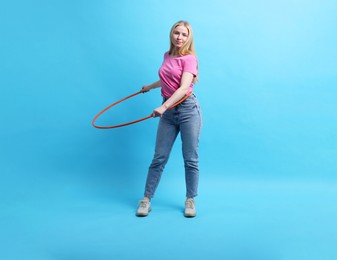 Photo of Beautiful young woman exercising with hula hoop on light blue background