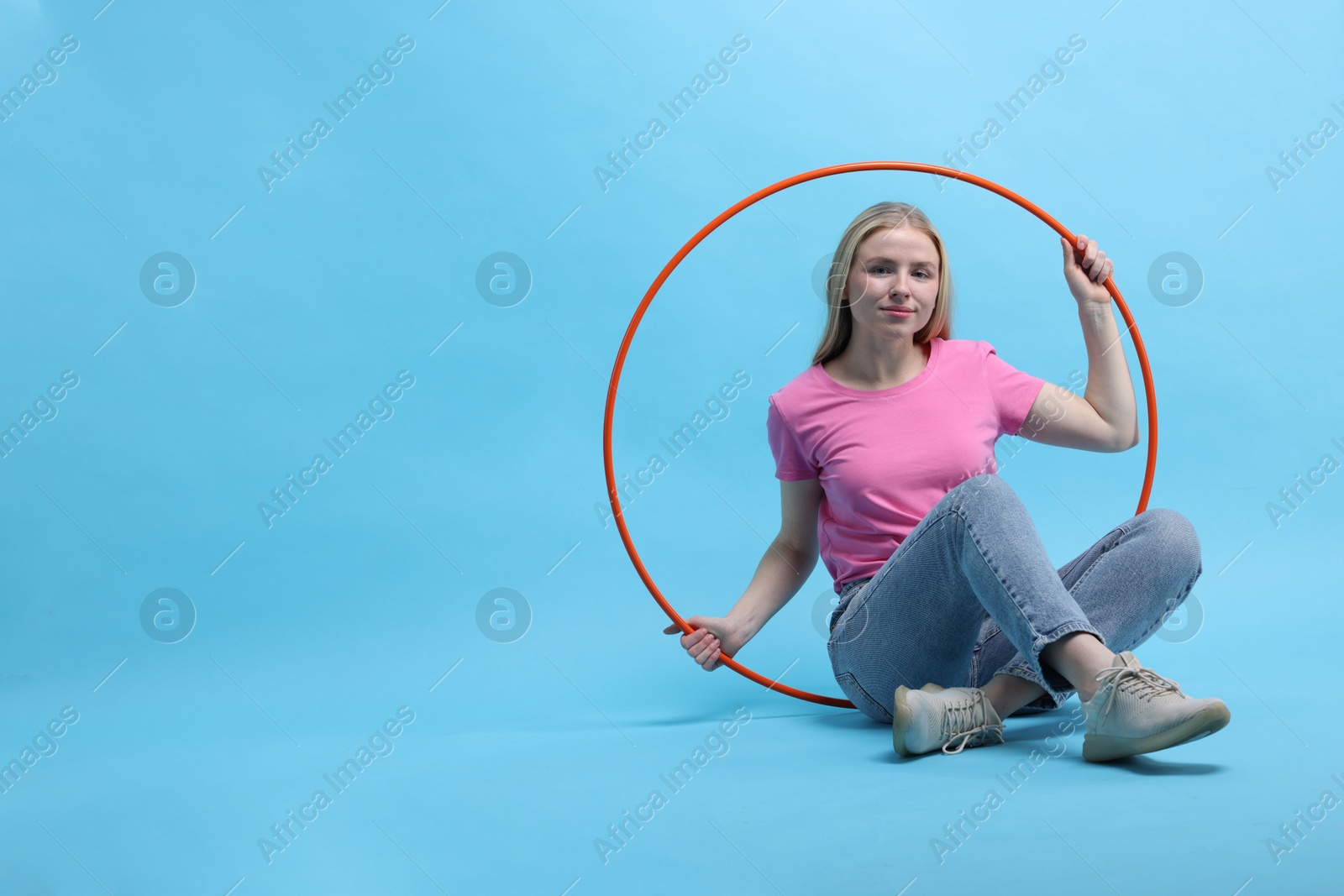 Photo of Beautiful young woman with hula hoop on light blue background, space for text