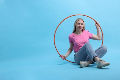 Photo of Beautiful young woman with hula hoop on light blue background, space for text